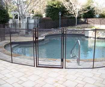 Brown mesh pool safety fence with self-closing gate enclosing curved backyard pool with stone coping and handrail